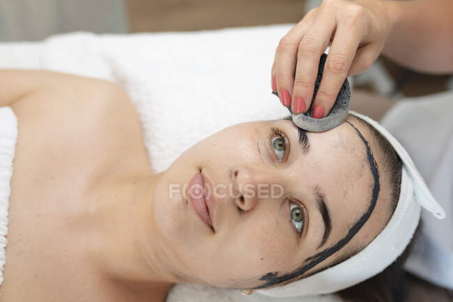 Mulher caucasiana deitada enquanto esteticista remove máscara facial. cliente desfrutando de tratamento em um salão de beleza. — Fotografia de Stock