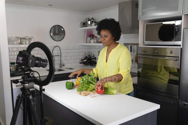 Африканская американка-блогер записывает видео на кухне. Рублю овощи. самоизоляция технологии связи в домашних условиях во время коронавируса ковид 19 пандемии. — стоковое фото