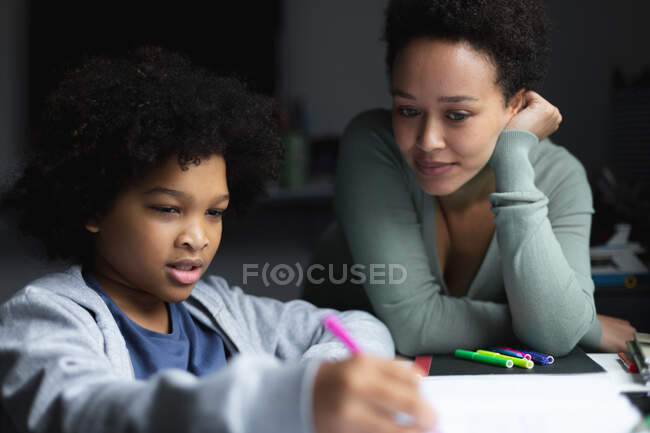 Mixed race woman watching daughter drawing in notebook. self isolation quality family time at home together during coronavirus covid 19 pandemic. — Stock Photo