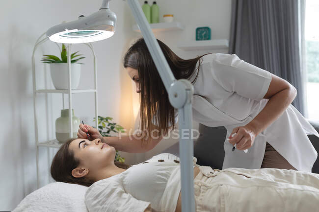 Mujer caucásica acostada mientras la esteticista se tiñe las cejas. cliente disfrutando del tratamiento en un salón de belleza. - foto de stock