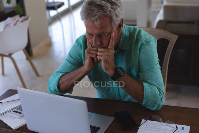 Hombre caucásico mayor preocupado sentado en la mesa usando el portátil pagando facturas. en casa en autoaislamiento durante coronavirus covid 19 pandemia de bloqueo - foto de stock