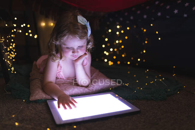 Menina caucasiana deitada no quarto usando tablet à noite. desfrutando de tempo de qualidade em casa durante coronavírus covid 19 bloqueio pandêmico. — Fotografia de Stock