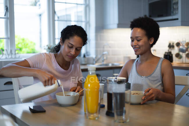 Gemischte Rasse gleichgeschlechtliche Frauen beim Frühstück in der Küche. Selbstisolierung Qualität Zeit zu Hause zusammen während Coronavirus covid 19 Pandemie. — Stockfoto