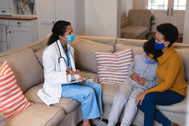 Mixed race mother and daughter talking to mixed race female doctor sitting on couch. self isolation at home together during coronavirus covid 19 pandemic. — Stock Photo