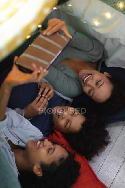 Happy mixed race lesbian couple and daughter lying down using smartphone. self isolation quality family time at home together during coronavirus covid 19 pandemic. — Stock Photo