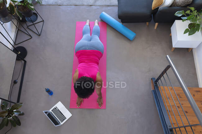 Femme afro-américaine utilisant un ordinateur portable faisant de l'exercice portant des vêtements de sport. auto-isolement technologie de conditionnement physique communication à la maison pendant le coronavirus covide 19 pandémie. — Photo de stock