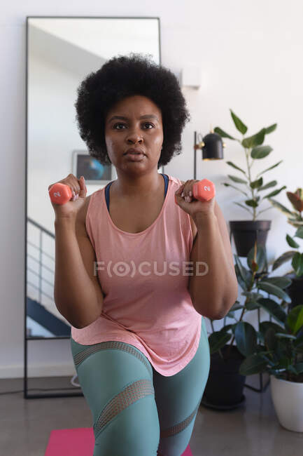 Portrait of african american woman working out using dumbbells. self isolation fitness at home during coronavirus covid 19 pandemic. — Stock Photo