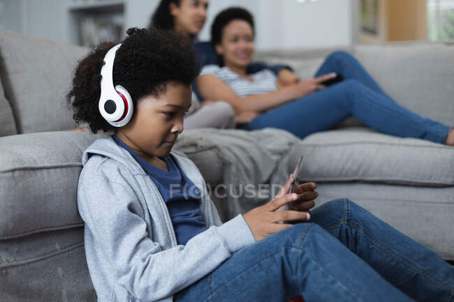 Chica de raza mixta sentada junto al sofá escuchando música. autoaislamiento calidad familia tiempo en casa juntos durante coronavirus covid 19 pandemia. - foto de stock