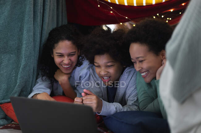 Lesbisches Paar und Tochter mit gemischter Rasse liegen mit Laptop in Deckenforts. Selbst-Isolation Qualität Familienzeit zu Hause zusammen während Coronavirus covid 19 Pandemie. — Stockfoto