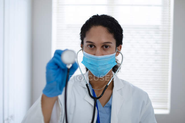 Портрет змішаної раси жінки-лікаря, який дивиться на камеру, що тримає стетоскоп. Якість самоізоляції вдома разом під час пандемії коронавірусу 19 . — стокове фото