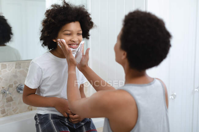 Frau mit gemischter Rasse spielt mit Tochter im Badezimmer Creme auf ihr Gesicht auftragen. Selbstisolierung Qualität Zeit zu Hause zusammen während Coronavirus covid 19 Pandemie. — Stockfoto