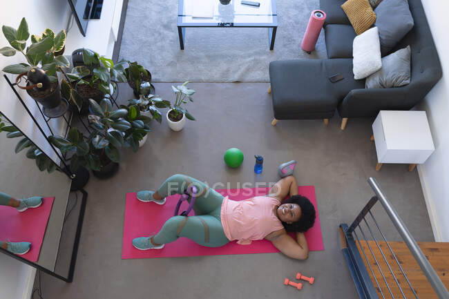 Blick von oben auf eine Afrikanerin, die auf einer Trainingsmatte liegt. Selbst-Isolation Fitness zu Hause während Coronavirus covid 19 Pandemie. — Stockfoto