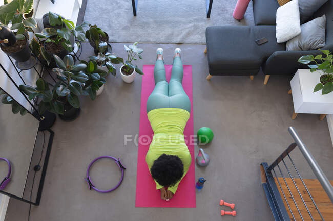 Overhead view of african american woman lying on exercise mat working out. self isolation fitness at home during coronavirus covid 19 pandemic. — Stock Photo