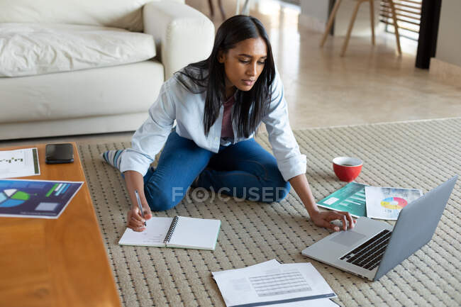 Gemischte Rasse Frau sitzt auf dem Boden mit Laptop und schreibt zu Hause. Selbstisolation während der Covid 19 Coronavirus-Pandemie. — Stockfoto