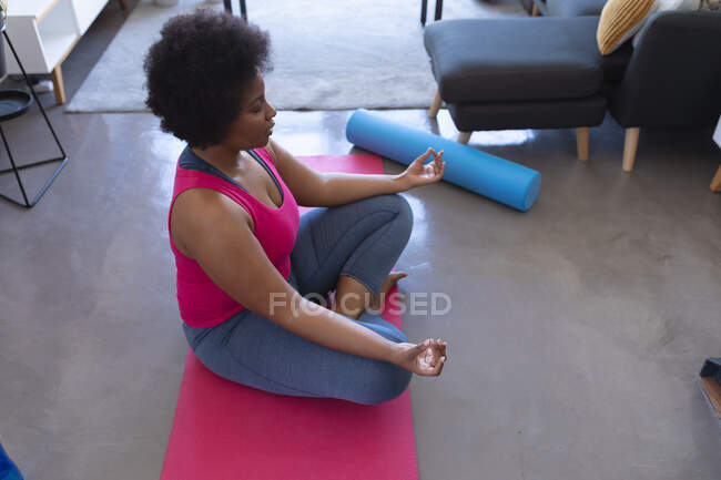 Africano americano mulher meditando sentado no tapete vestindo roupas esportivas. auto isolamento fitness bem-estar em casa durante coronavírus covid 19 pandemia. — Fotografia de Stock