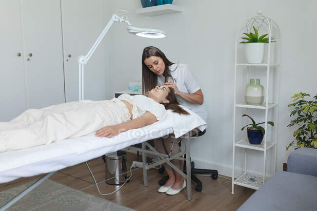 Femme blanche allongée pendant que l'esthéticienne examine son visage. client bénéficiant d'un traitement dans un salon de beauté. — Photo de stock