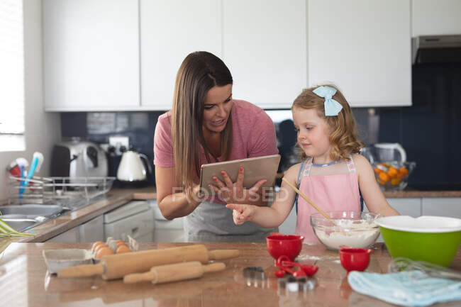 Caucasiano mãe e filha assar na cozinha usando tablet. desfrutando de tempo de qualidade em casa durante coronavírus covid 19 bloqueio pandêmico. — Fotografia de Stock