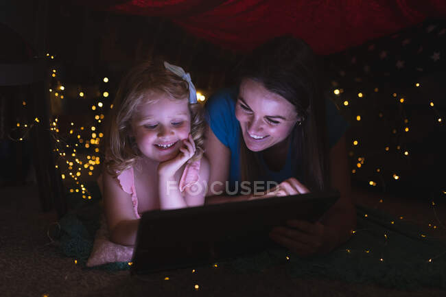 Кавказская мать и дочь, имеющие в спальне с помощью цифрового планшета и улыбаясь. наслаждаясь временем дома во время коронавирусного ковида 19 пандемического блокирования. — стоковое фото