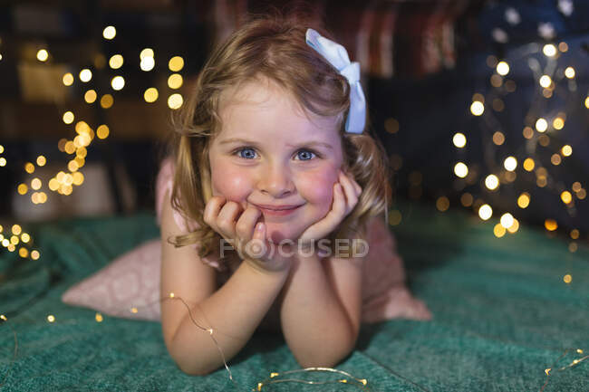 Portrait de fille caucasienne couchée sur une couverture verte dans la chambre. regardant la caméra et souriant. profiter d'un temps de qualité à la maison pendant le confinement de coronavirus covid 19 pandémie. — Photo de stock