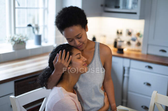 Feliz mestiço casal feminino abraçando na cozinha pela manhã. auto isolamento tempo de qualidade em casa juntos durante coronavírus covid 19 pandemia. — Fotografia de Stock