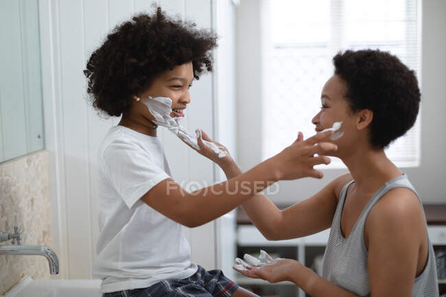 Donna razza mista che gioca con la figlia in bagno. mettendole della panna in faccia. auto isolamento tempo di qualità a casa insieme durante coronavirus covid 19 pandemia. — Foto stock