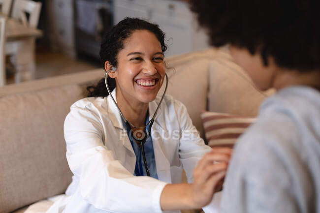 Chica de raza mixta que está siendo examinada por una doctora de raza mixta. autoaislamiento calidad tiempo en casa juntos durante coronavirus covid 19 pandemia. - foto de stock