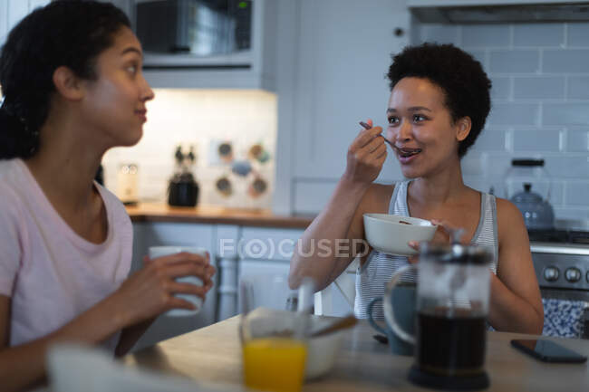 Mixed race same sex female couple eating breakfast in kitchen. self isolation quality time at home together during coronavirus covid 19 pandemic. — Stock Photo