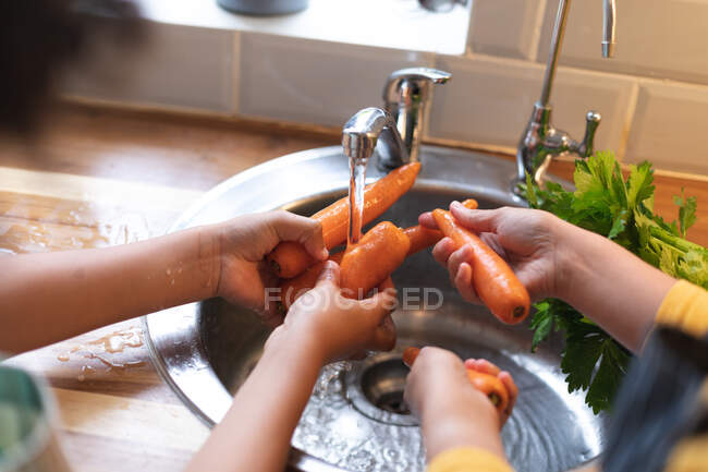 Pareja preparando comida lavando zanahorias en fregadero de cocina. autoaislamiento calidad familia tiempo en casa juntos durante coronavirus covid 19 pandemia. - foto de stock