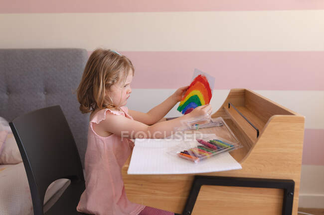 Caucasian girl holding drawing, sitting at desk at home. enjoying quality time at home during coronavirus covid 19 pandemic lockdown. — Stock Photo