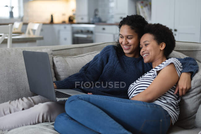 Lesbisches Paar mit gemischter Rasse sitzt mit Laptop auf der Couch. Selbst-Isolation Qualität Familienzeit zu Hause zusammen während Coronavirus covid 19 Pandemie. — Stockfoto