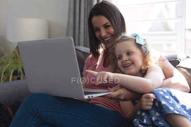 Кавказька мати і дочка добре лежатимуть на дивані за допомогою ноутбука. Якісний час, проведений під час коронавірусного ув 