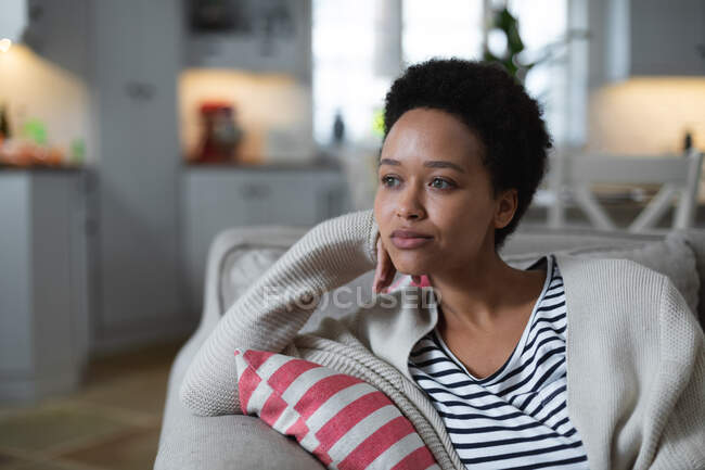 Жінка змішаної раси, що сидить на дивані, виглядає сумно. самоізоляція якість сімейного часу вдома разом під час пандемії коронавірусу 19 . — стокове фото