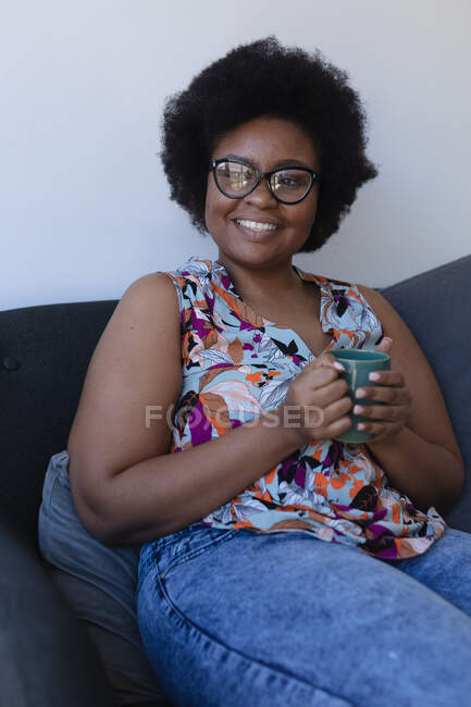 В середині афроамериканської жінки, яка сидить на дивані і п'є каву. Самоізоляція вдома під час коронавірусу (19 пандемії). — стокове фото