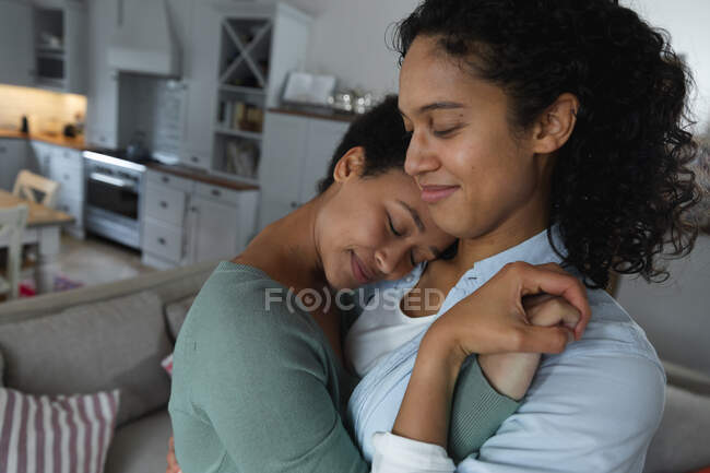 Romántica pareja de lesbianas mestizas bailando en la sala de estar. autoaislamiento calidad tiempo en casa juntos durante coronavirus covid 19 pandemia. - foto de stock