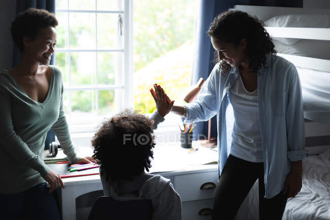 Mixed race lesbian couple and daughter high fiving. self isolation quality family time at home together during coronavirus covid 19 pandemic. — Stock Photo