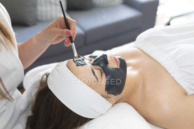 Donna caucasica sdraiata mentre estetista applica una maschera facciale. cliente che si gode il trattamento in un salone di bellezza. — Foto stock