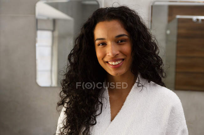 Portrait of mixed race woman in bathroom smiling to camera. looking at the camera and smiling. self isolation at home during covid 19 coronavirus pandemic. — Stock Photo