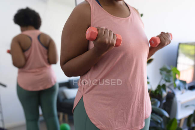 Midesction di donna afro-americana che lavora con i manubri. auto isolamento fitness a casa durante il coronavirus covid 19 pandemia. — Foto stock