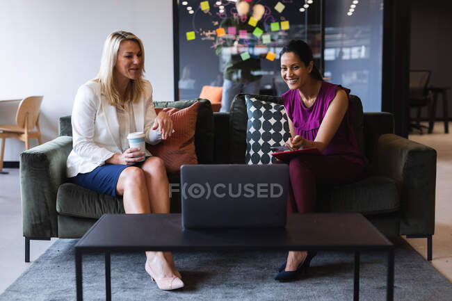 Различные деловые женщины, пьющие кофе с помощью ноутбука во время видеозвонка в креативный офис. современные технологии бизнес-бизнес-бизнес-штурм. — стоковое фото