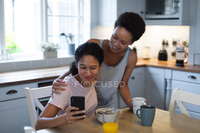 Mixed race female couple taking a selfie during breakfast in kitchen. self isolation quality time at home together during coronavirus covid 19 pandemic. — Stock Photo