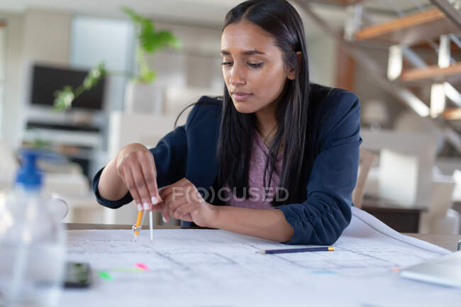 Жінка змішаної раси сидить за столом, використовуючи компас, що працює вдома. самоізоляція під час пандемії коронавірусу 19 . — стокове фото
