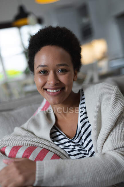 Femme de race mixte assis sur le canapé regardant la caméra et souriant. auto isolement qualité famille temps à la maison ensemble pendant coronavirus covid 19 pandémie. — Photo de stock
