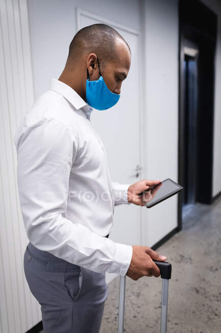 Homme de race mixte portant un masque facial dans un bureau. en utilisant une tablette numérique. petite entreprise créative pendant la pandémie de coronavirus covid 19. — Photo de stock