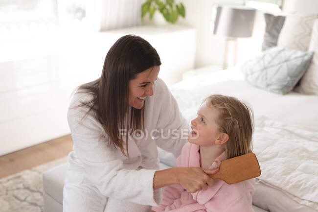 Femme et fille caucasiennes s'amusent dans la chambre. Mère brosse les cheveux de sa fille. profiter d'un temps de qualité à la maison pendant le confinement de coronavirus covid 19 pandémie. — Photo de stock