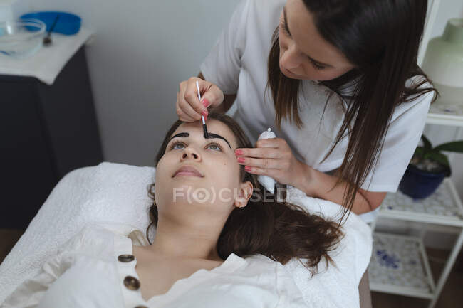 Кавказька жінка лягла спиною, а красуня фарбувала брови. Клієнт отримує задоволення від лікування в салоні краси.. — стокове фото