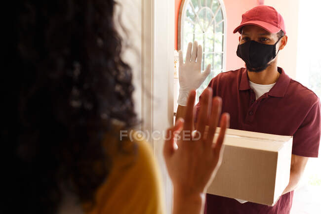 Mixed race woman wearing face mask receiving a package. self isolation during covid 19 coronavirus pandemic — Stock Photo
