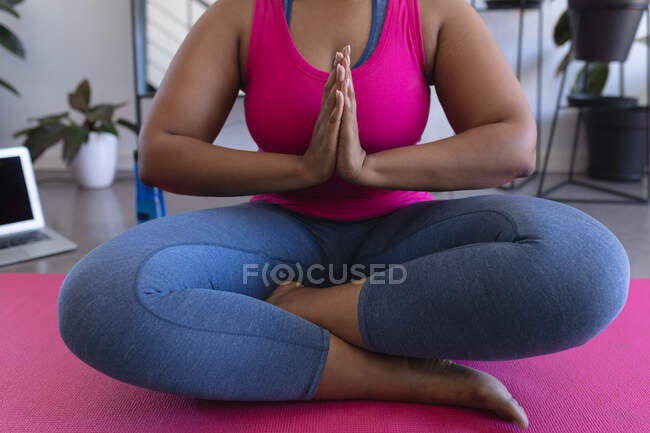Midsection of african american woman meditating wearing sports clothes. self isolation fitness at home during coronavirus covid 19 pandemic. — Stock Photo