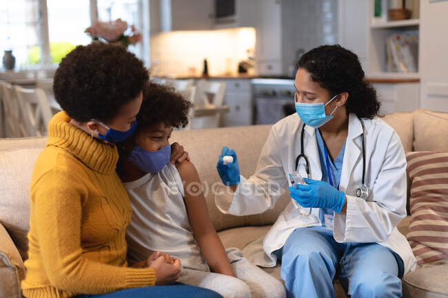 Mädchen mit gemischter Rasse und Mutter mit Mundschutz und Ärztin mit gemischter Rasse, die Grippeimpfung vorbereitet. Selbstisolation zu Hause während Coronavirus covid 19 Pandemie. — Stockfoto