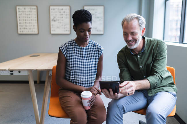 Diverse man and woman drinking coffee using digital tablet in creative office. technology modern office business teamwork brainstorming. — Stock Photo