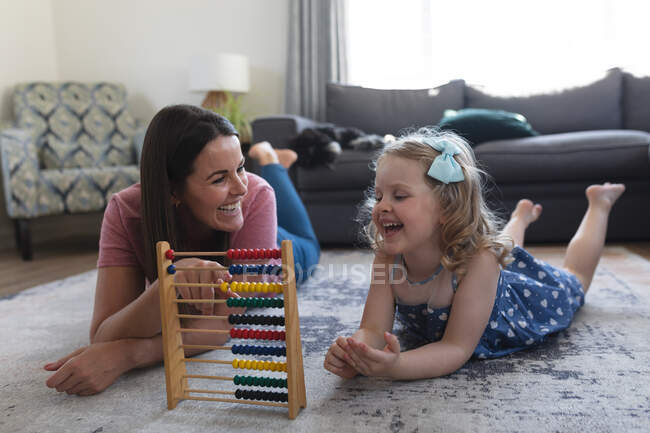Caucasian mother and daughter having fun lying in living room. playing with an abacus. enjoying quality time at home during coronavirus covid 19 pandemic lockdown. — Stock Photo